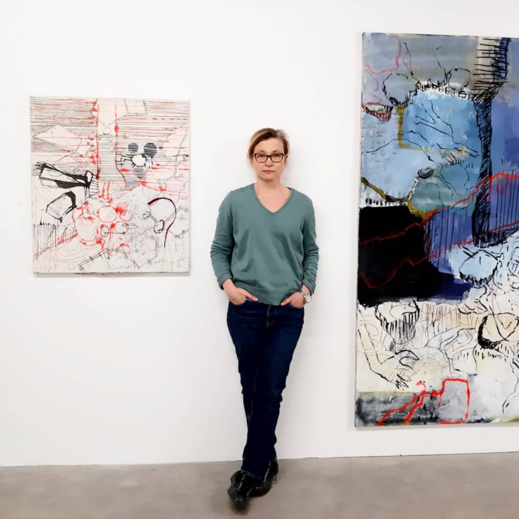 Artist, Naomi Middelmann posing next to her paintings.
